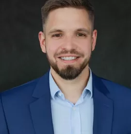 Mężczyzna w niebieskim garniturze uśmiecha się na ciemnym tle.