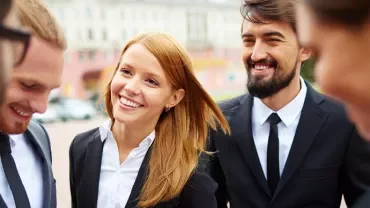 Group of professionals smiling in business attire outdoors.