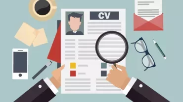 Ilustracja przedstawiająca dłonie trzymające CV z lupą, smartfonem, okularami i przyborami biurowymi na biurku.