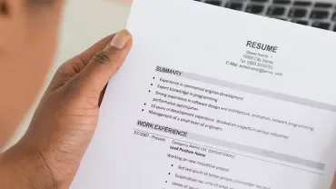 Person reviewing a printed resume with summary and work experience sections visible.
