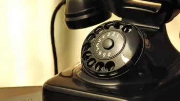 Zabytkowy czarny telefon z tarczą obrotową na stole.