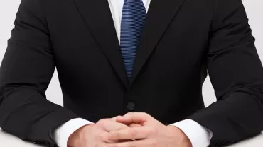 Mężczyzna w garniturze z dłońmi na stole.