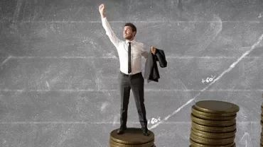 Man standing on coins, chalkboard graph in background