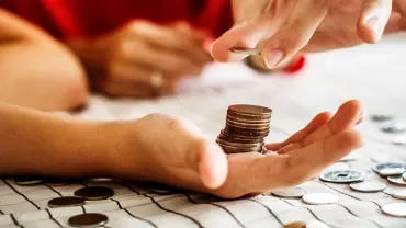 Hand holding coins, stacking more on a table.