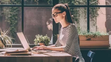 Kobieta w okularach pracująca na laptopie przy oknie.