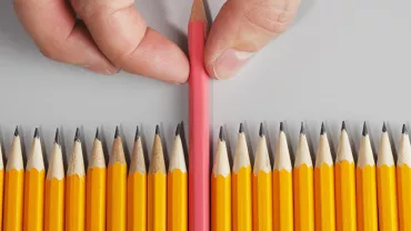 Person picking a red pencil among yellow pencils.