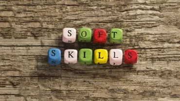 Kolorowe koraliki układające się w napis 'Soft Skills' na tle drewna.