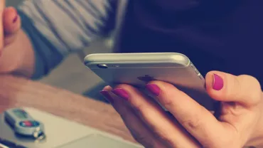 Osoba trzymająca smartfon z laptopem i pendrive'em na stole.