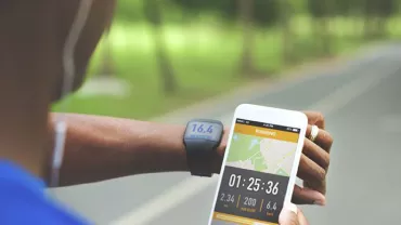 Osoba sprawdzająca statystyki biegania na telefonie i smartwatchu