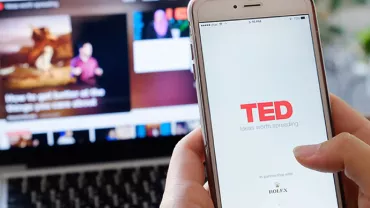Osoba używająca aplikacji TED na smartfonie z laptopem w tle.