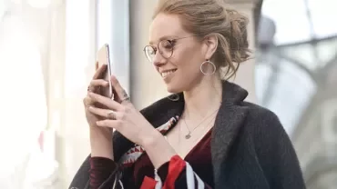 Kobieta uśmiecha się, patrząc na swój smartfon.