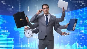 Biznesmen z wieloma ramionami trzymającymi laptopa, teczkę, zegar i telefon w tle wykresów.