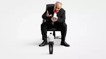A large man in a suit scolds a smaller man through a megaphone.