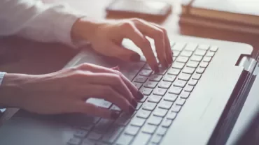 Osoba pisząca na klawiaturze laptopa.