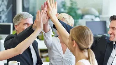 Grupa profesjonalistów robiących 'high five' w biurze.