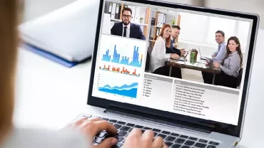 Wideokonferencja na laptopie z wykresami i uczestnikami.