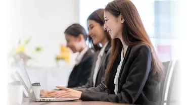 Trzy kobiety w strojach biznesowych pracujące na laptopach w biurze.