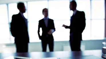 Trzy rozmazane postacie w sali konferencyjnej z dużymi oknami.