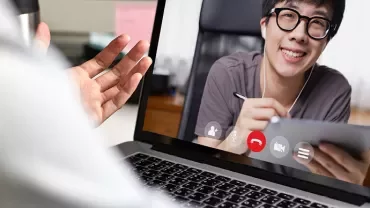 Osoba na wideorozmowie, używająca laptopa, uśmiechnięta w słuchawkach.