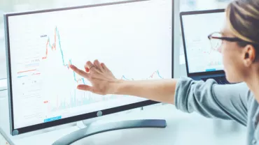 Osoba analizująca wykresy finansowe na ekranie komputera.
