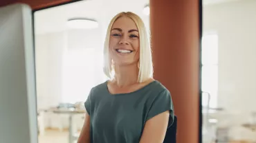 Uśmiechnięta kobieta przy biurku w nowoczesnym biurze.
