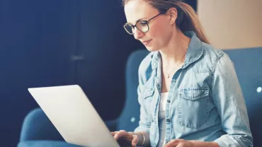 Kobieta w okularach używająca laptopa na kanapie.