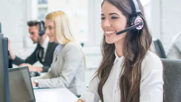 Kobieta z zestawem słuchawkowym uśmiecha się przy komputerze w call center.