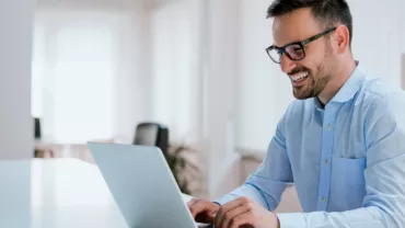 A man sitting down smiling at laptop in front of him