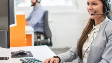 A woman sitting in front of the computer with headphones on, smiling