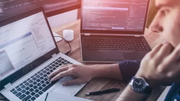 Osoba programująca na laptopie z kilkoma ekranami wyświetlającymi kod.
