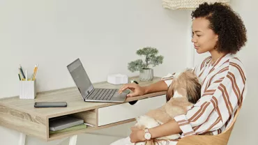 Kobieta pracuje na laptopie w domu z psem na kolanach.