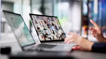 Osoba używająca laptopa do wideokonferencji w nowoczesnym biurze.