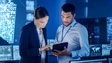Kobieta z mężczyzną patrzą na tablet w biurze z komputerami