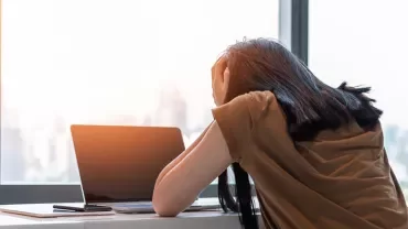 Person stressed at desk with laptop by window.