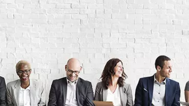 A diverse group of people sitting against a white brick wall.