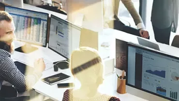 People in an office working at computers with charts displayed on screens.