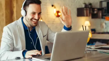 Man smiling and waving during a video call on a laptop.