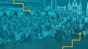 Duża grupa ludzi pozująca na zewnątrz z panoramą miasta w tle.