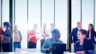 Business people interacting in a bright office with large windows.