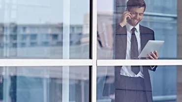 Businessman using tablet and phone behind glass window.