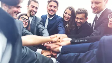 Group of businesspeople joining hands in a circle, smiling.