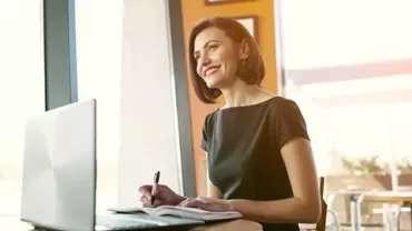 Woman smiling while working on a laptop in a cafe.