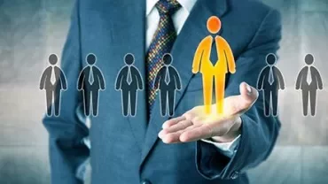 A businessman holding a glowing figure, symbolizing leadership amidst a row of grey silhouettes.