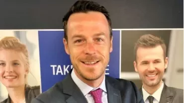 Man in suit with two smiling people on a poster in the background.