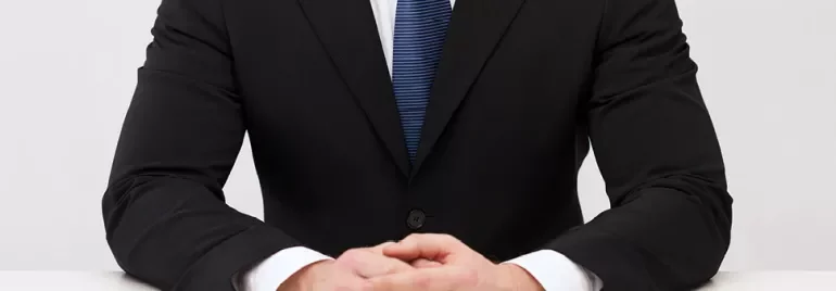 Mężczyzna w garniturze z dłońmi na stole.