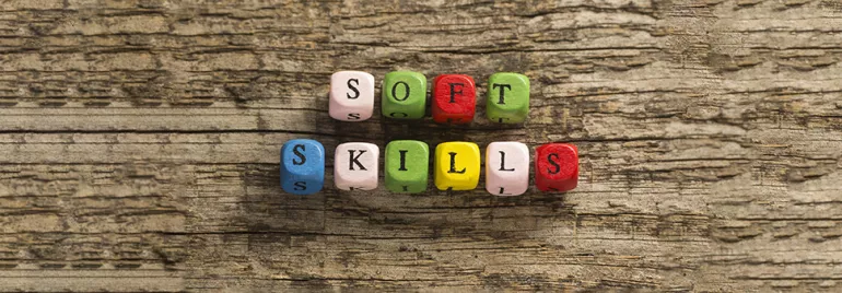 Kolorowe koraliki układające się w napis 'Soft Skills' na tle drewna.