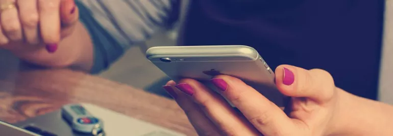 Osoba trzymająca smartfon z laptopem i pendrive'em na stole.