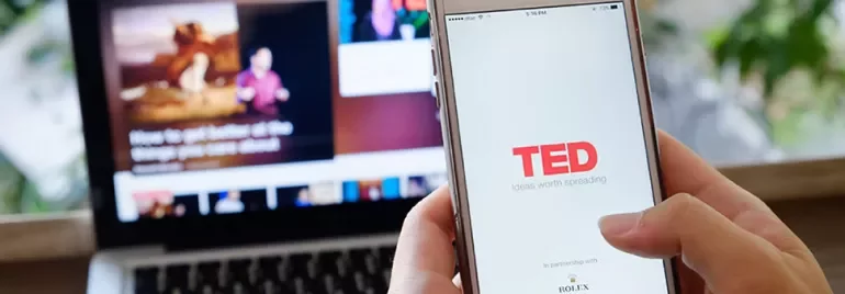 Osoba używająca aplikacji TED na smartfonie z laptopem w tle.