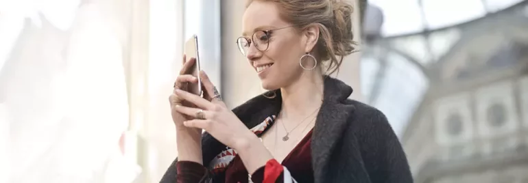 Kobieta uśmiecha się, patrząc na swój smartfon.
