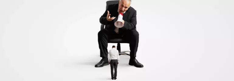 A large man in a suit scolds a smaller man through a megaphone.